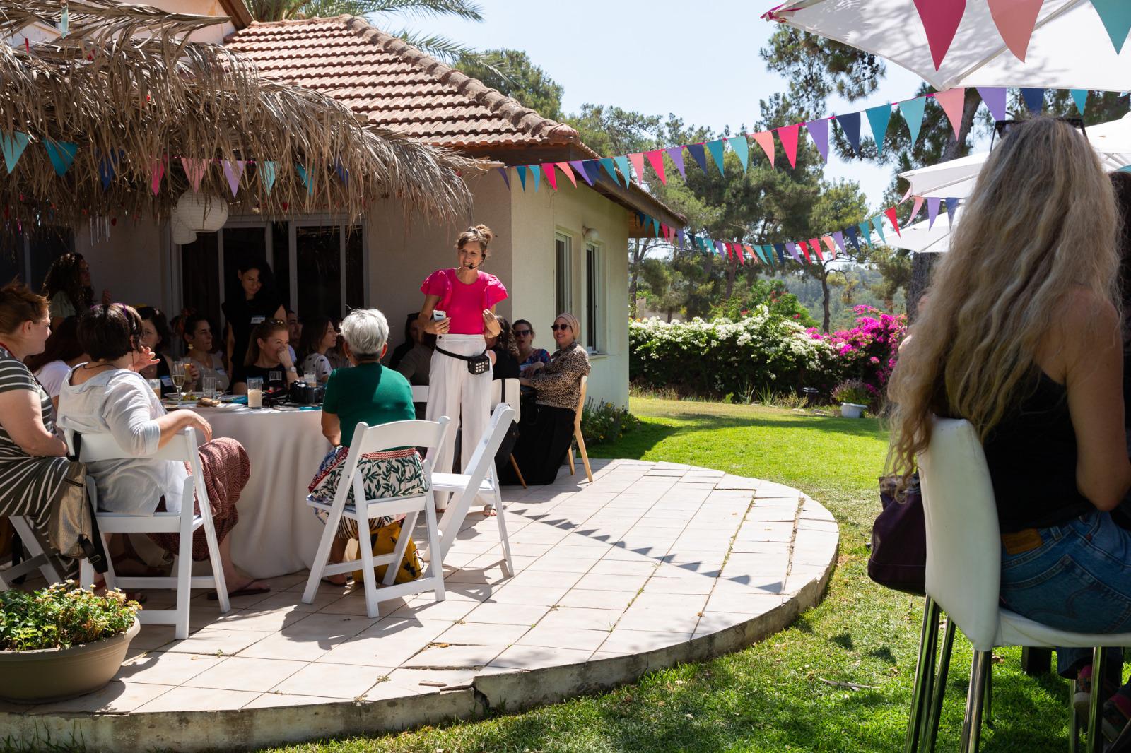 רונית כפיר בהרצאה בחצר הבית שלה עם נשים שיושבות סביב שולחן