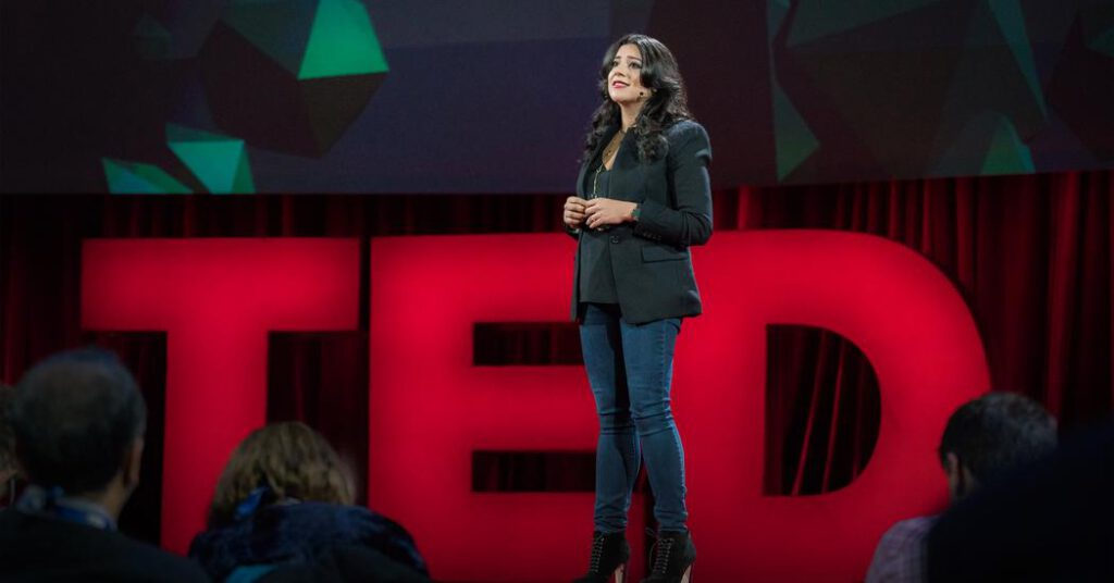 אישה לובשת שחור עובדת ומרצה מול קהל על במת TED