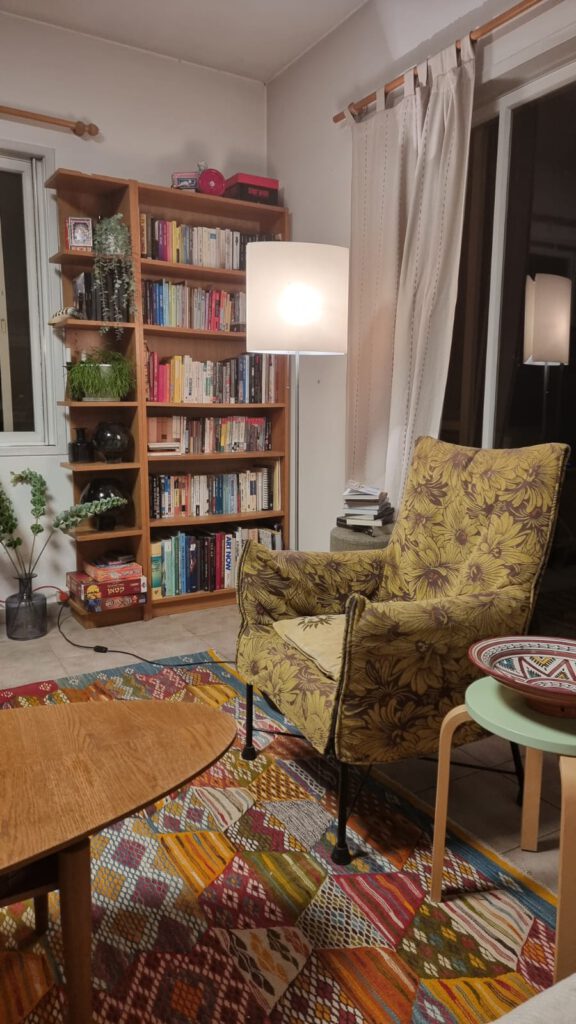 פינת ישיבה בסלון של רונית, רואים כורסא וכוננית הספרים המסודרת